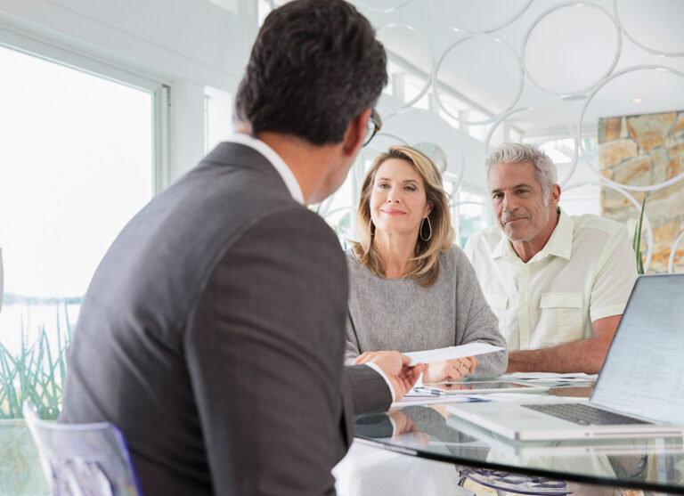 couple reviewing paperwork with a professional advisor seated at a desk with a laptop