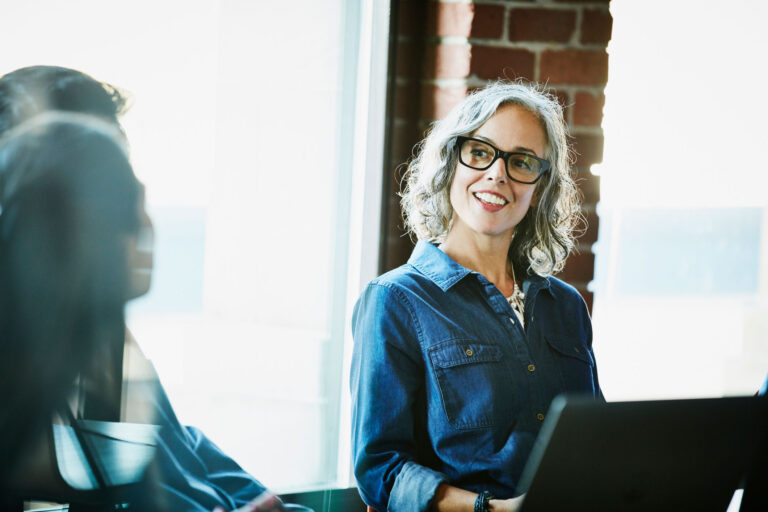 woman with glasses smiling toward couple over a computer screen