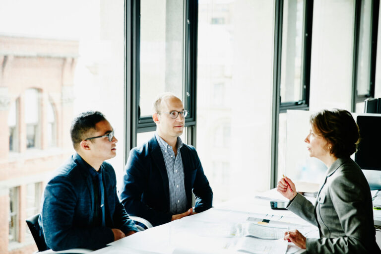 business woman leading a meeting seated across the table from two business men