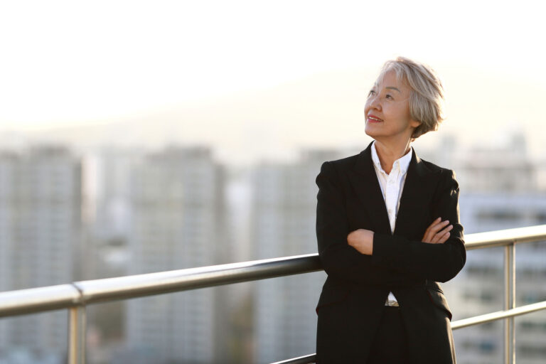 woman in suit with arms crossed and smiling looking toward sky