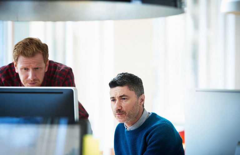 two men dressed in business casual studying a computer monitor display closely