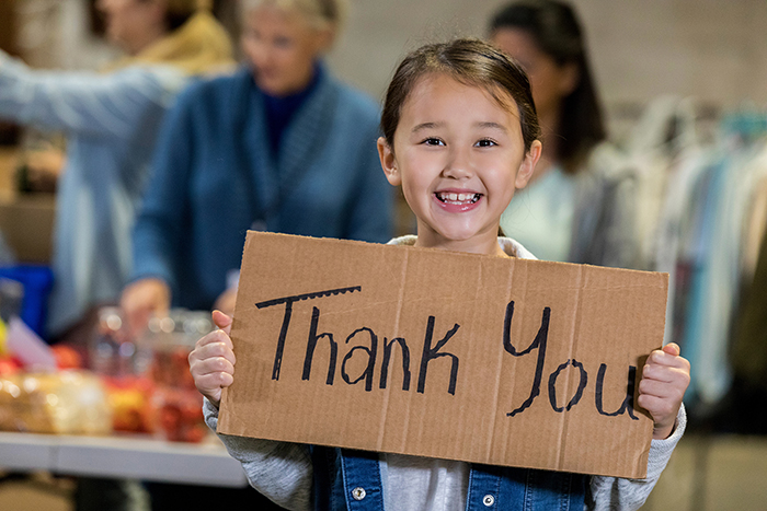 little girl smiling and holding up a thank you sign drawn on cardboard